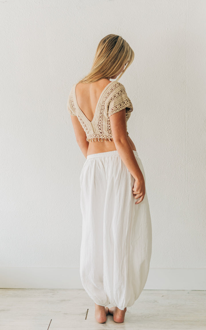 Woman wearing a lace top and white pants standing in a minimalistic room.