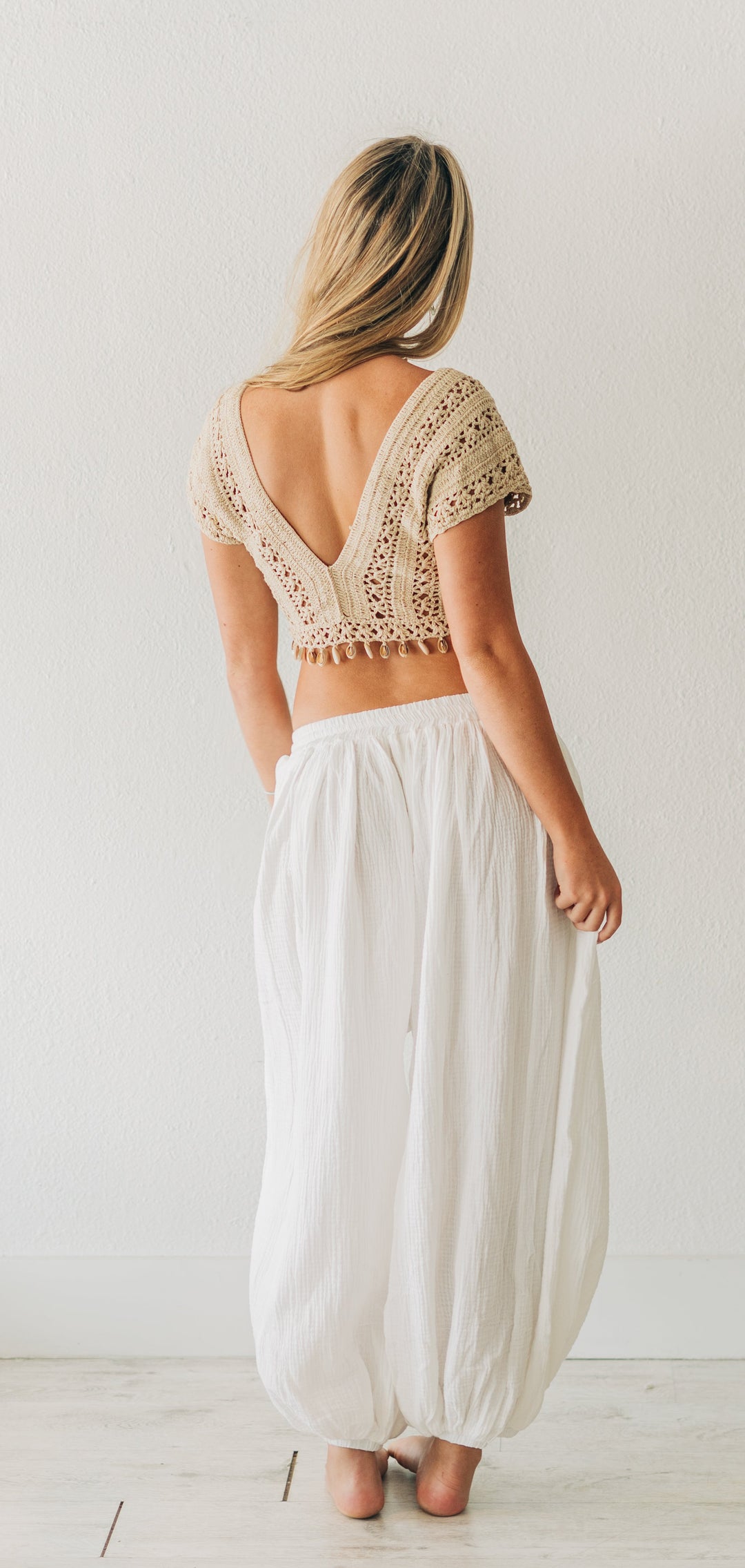 Woman wearing a lace top and white pants in a minimalistic room.