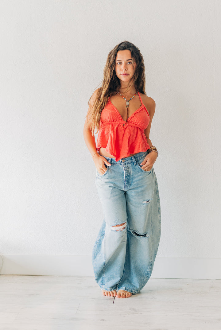 Woman wearing a red top and light blue jeans standing in a minimalistic room.