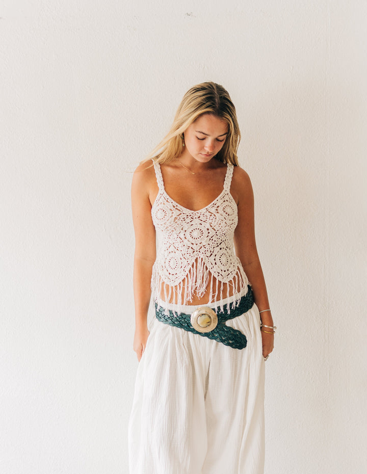 Woman wearing a white lace top and high-waisted pants with a belt in a minimalistic room.