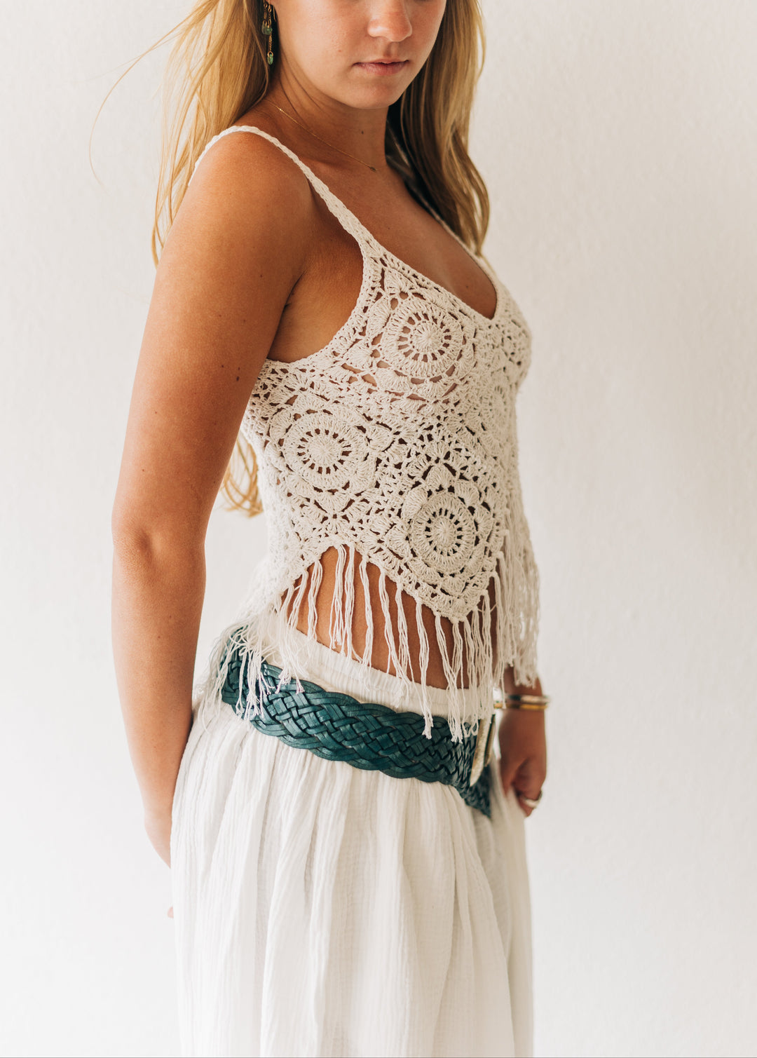 Woman wearing a crochet top with fringe details on a plain background