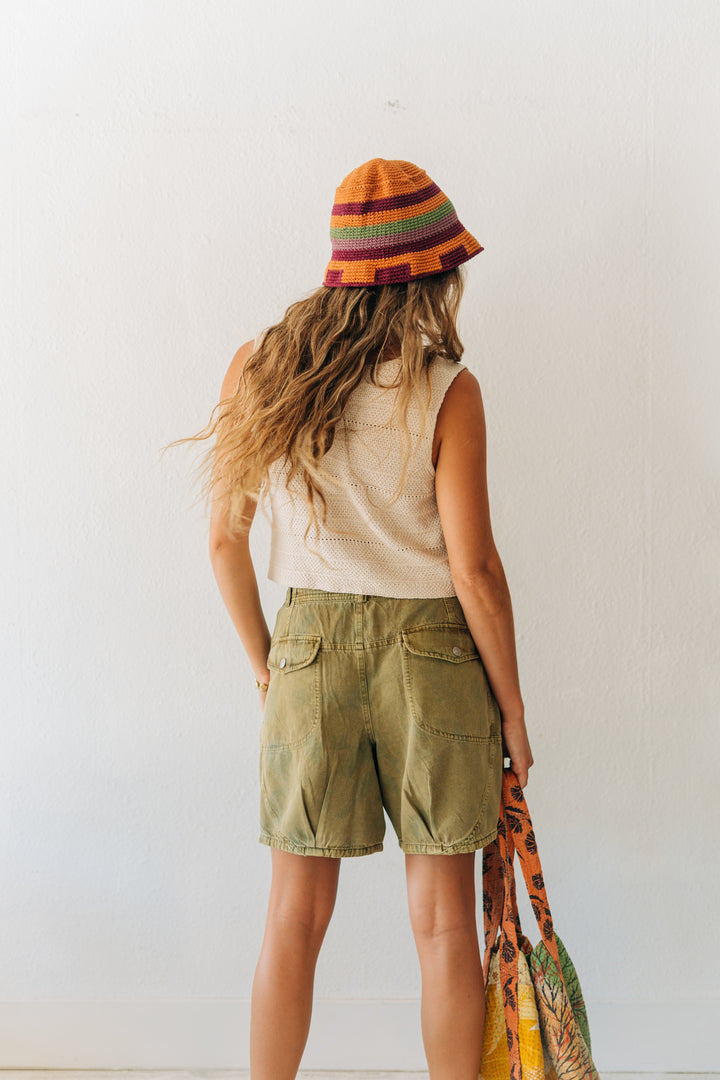 Person wearing a colorful striped hat and green shorts against a white wall