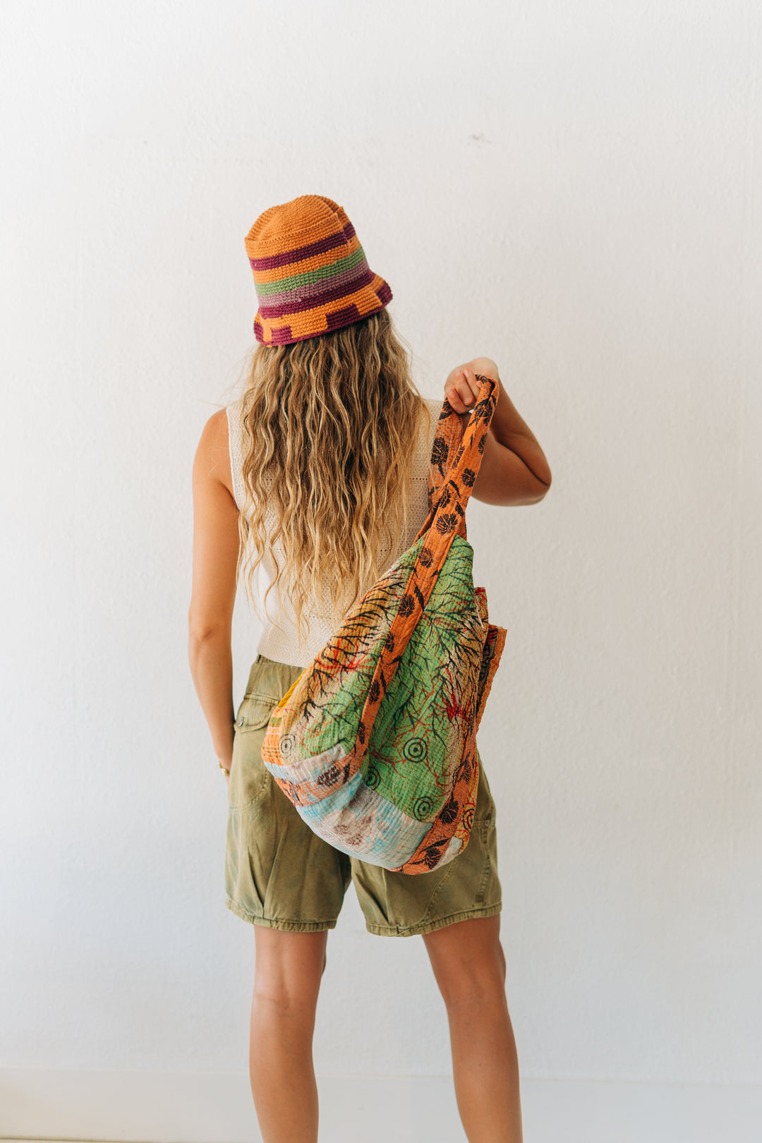 Person wearing a colorful beanie and holding a patterned bag against a white background