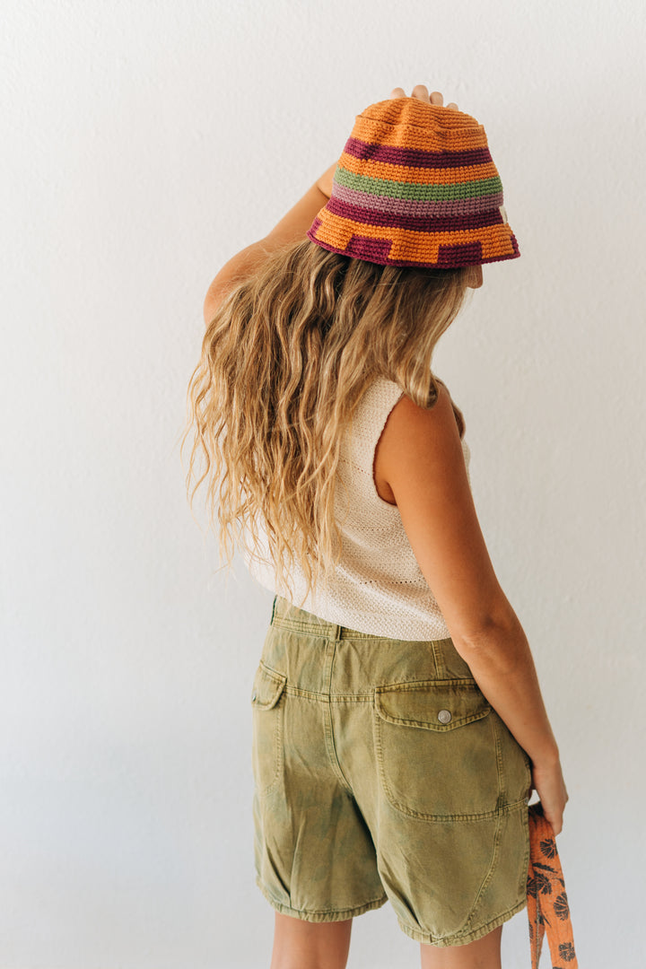 Person wearing a colorful striped bucket hat and green shorts against a white background