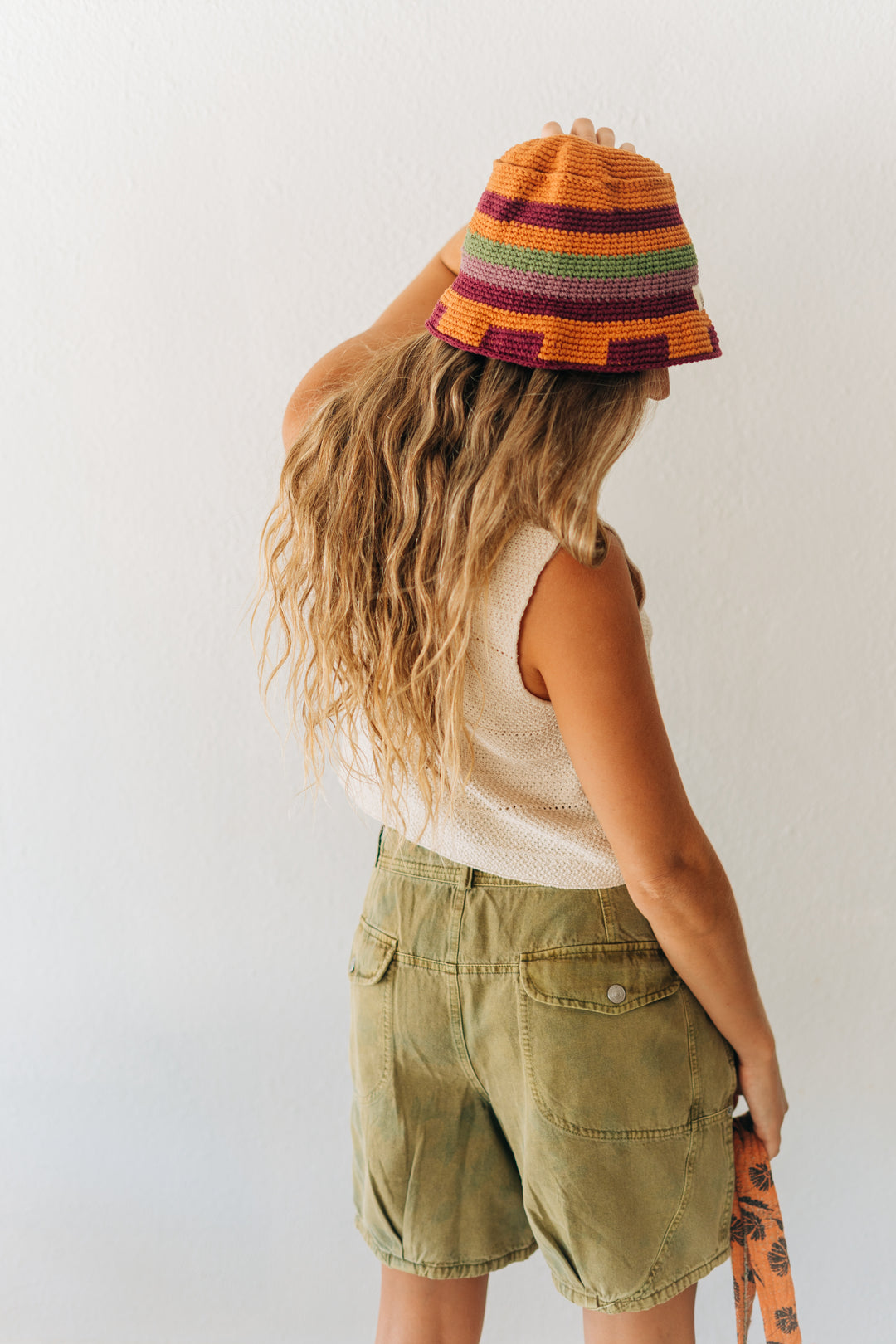 Person wearing a colorful striped bucket hat and green shorts against a white background