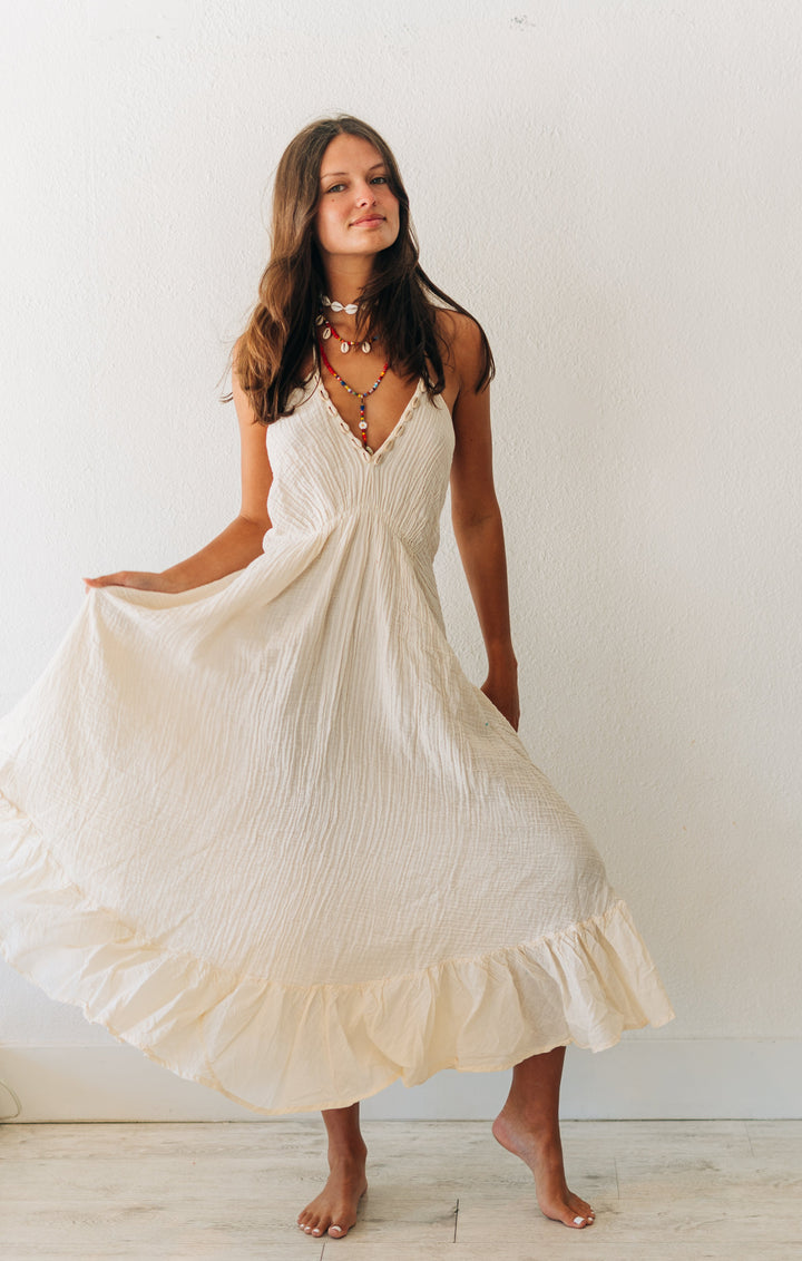 Woman in a white dress standing against a plain white wall.