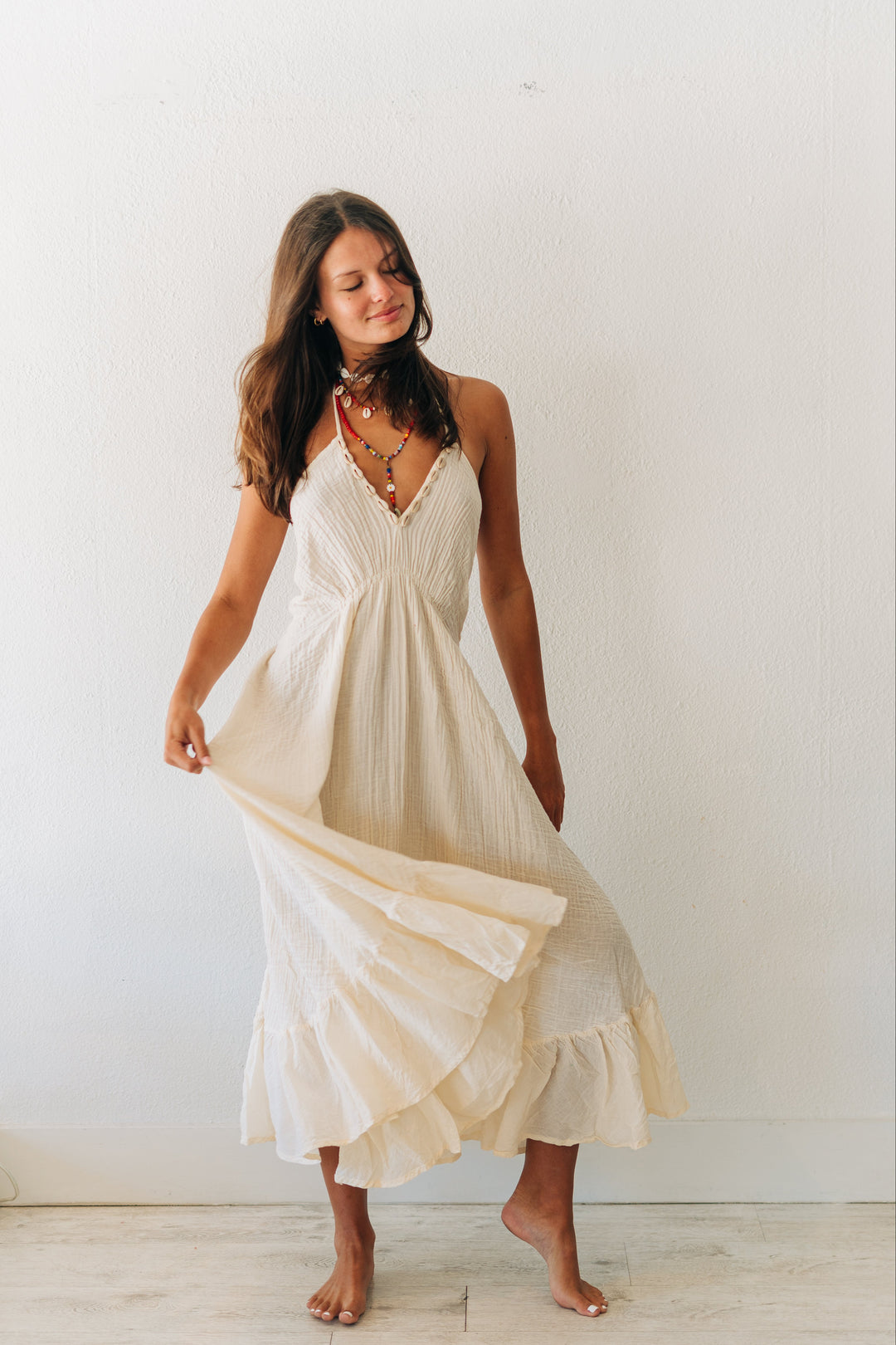 Woman wearing a flowing white dress against a plain white wall.