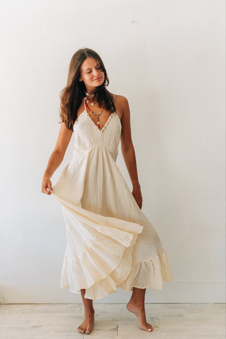 Woman wearing a flowing white dress against a plain white wall.