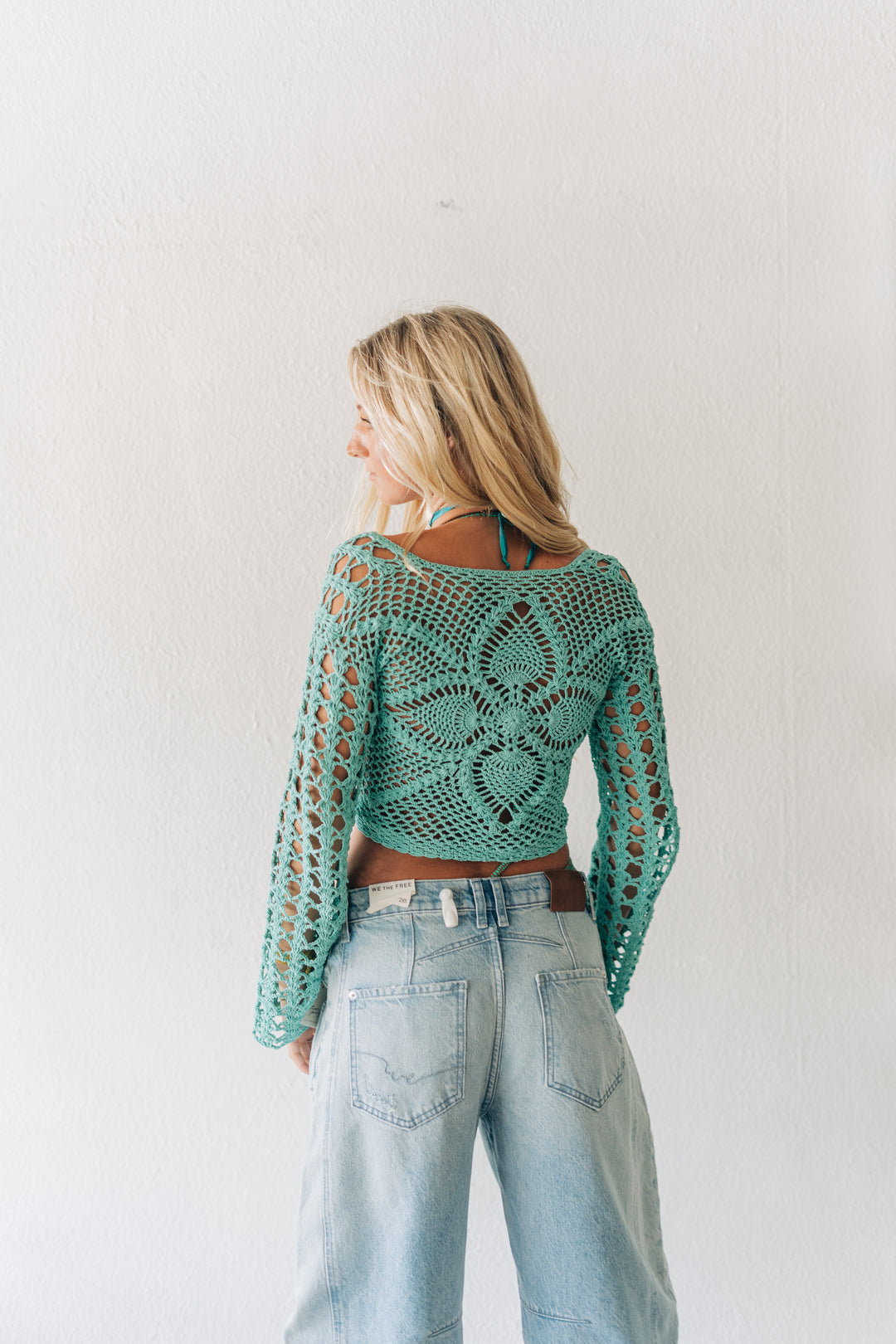 Woman wearing a teal crochet top and light blue jeans against a white background