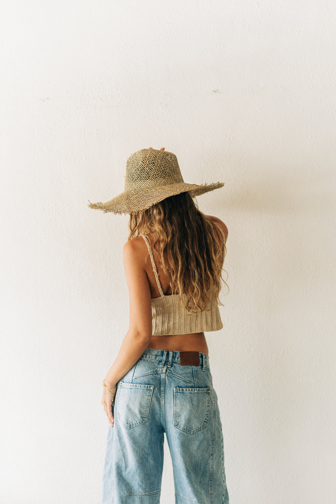 Person wearing a straw hat, crop top, and jeans against a plain background