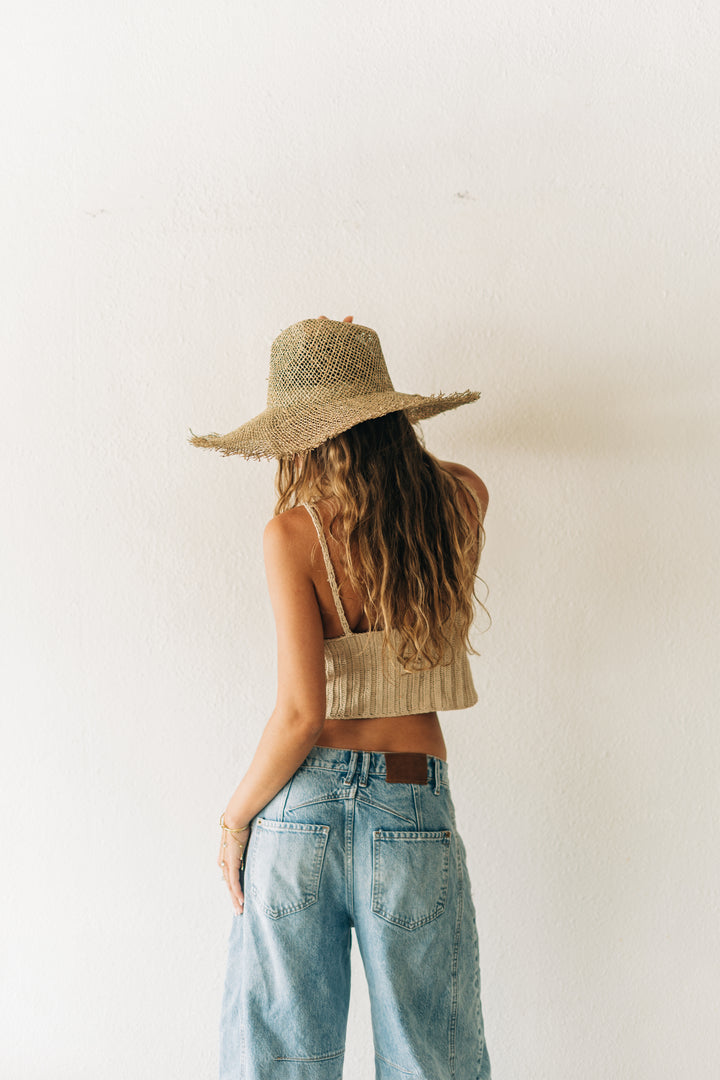 Person wearing a straw hat, crop top, and jeans against a plain background