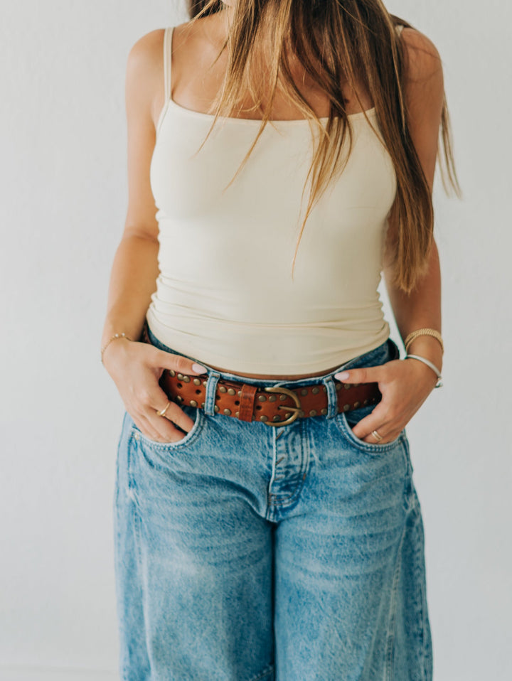 Woman wearing a white tank top and blue jeans against a plain background