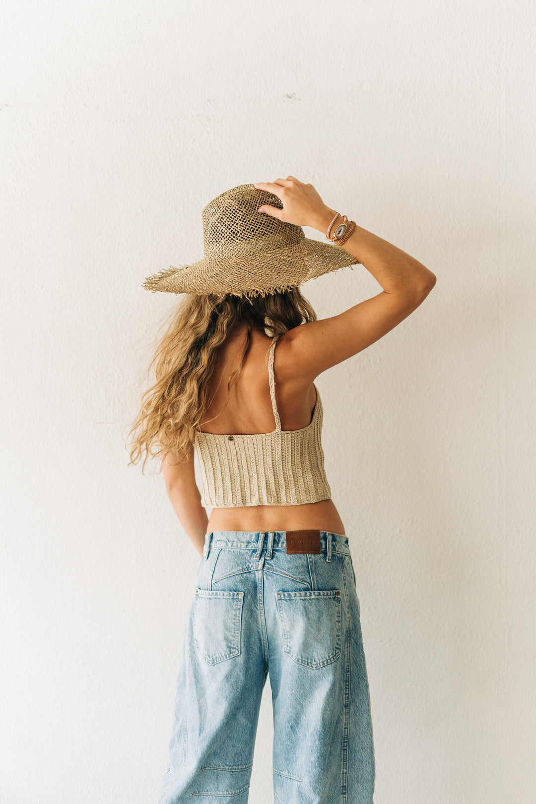 Person wearing a straw hat, beige crop top, and light blue jeans against a white background