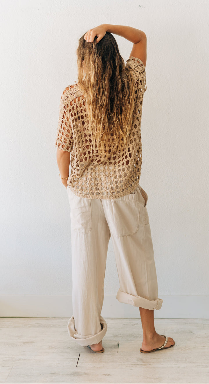 Person wearing a patterned top and light-colored pants against a white wall.