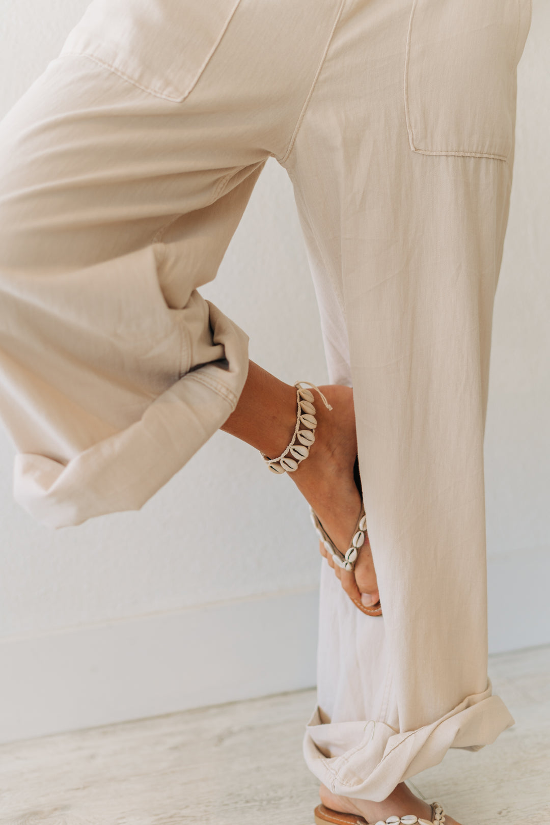 Person wearing beige pants and sandals on a light wooden floor.