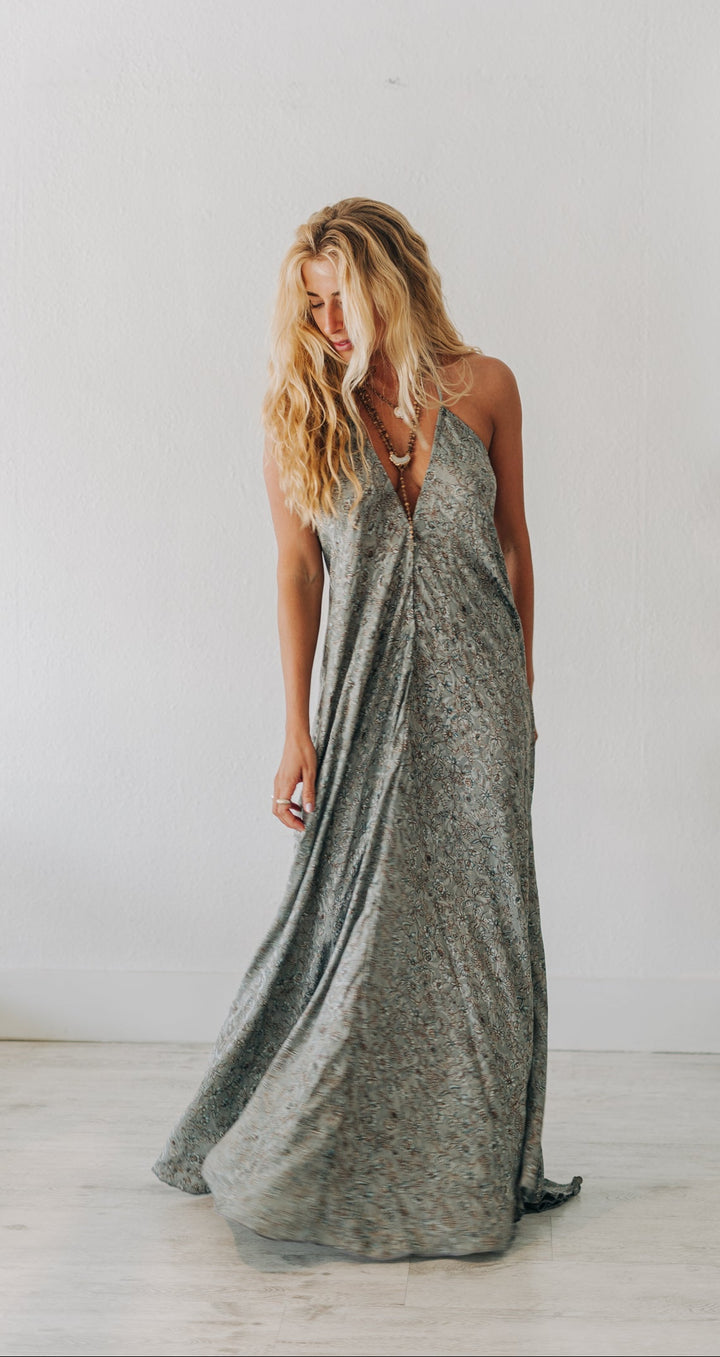 Woman wearing a long, patterned dress standing in a minimalistic room.