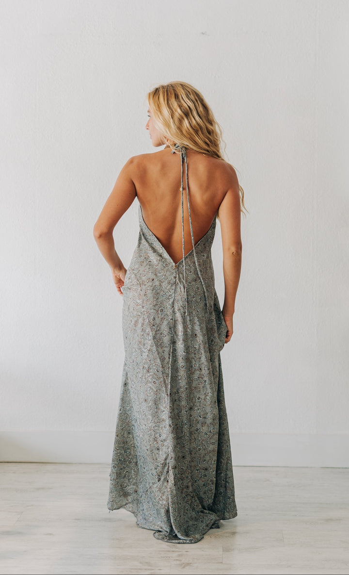 Woman wearing a long, light-colored dress with thin straps in a minimalistic room.