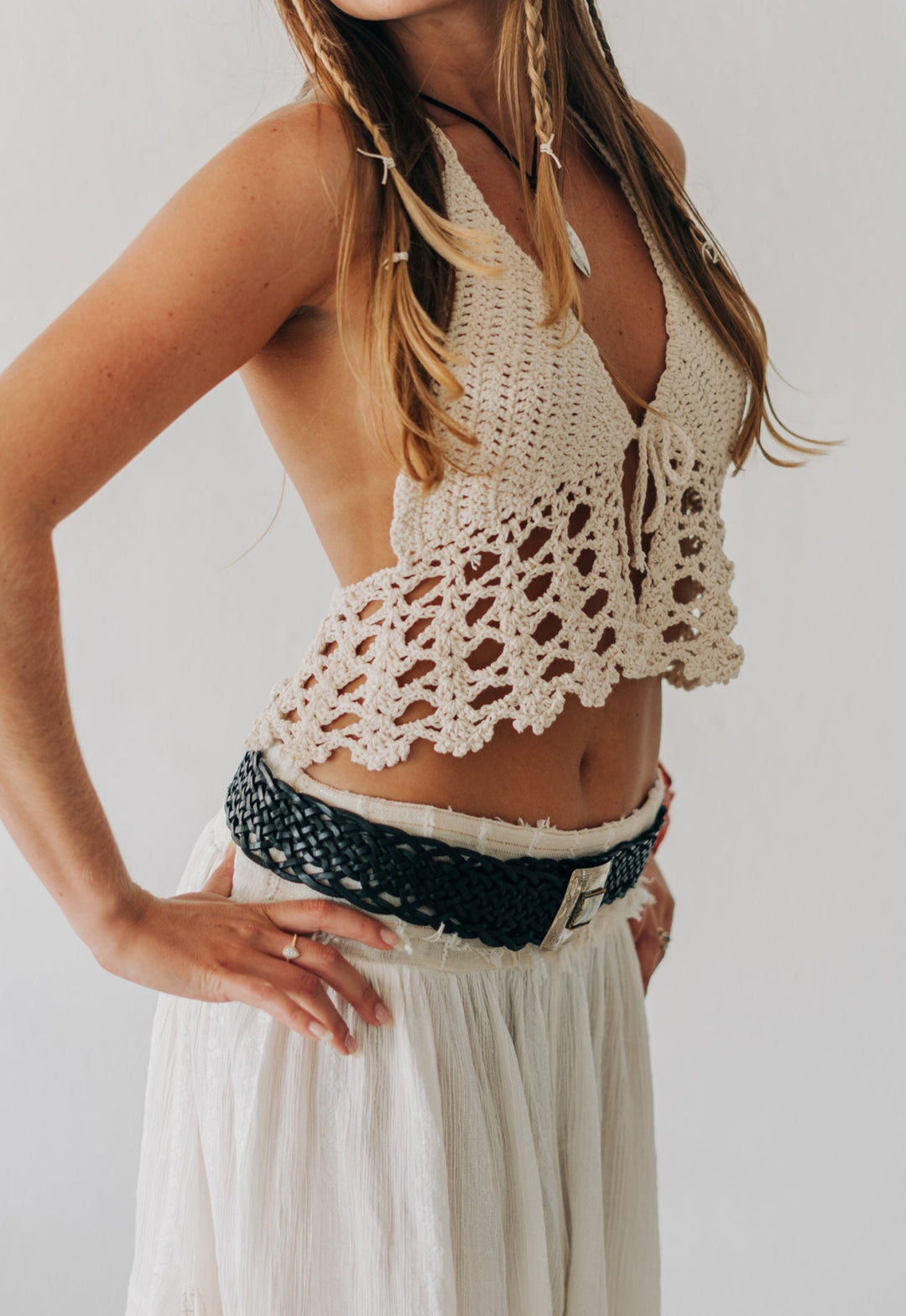 Woman wearing a crochet top and white pants against a plain background