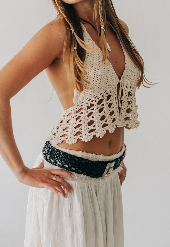 Woman wearing a crochet top and white pants against a plain background