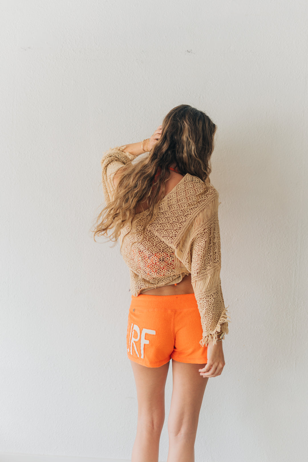 Person wearing a beige knit cardigan and orange shorts with &