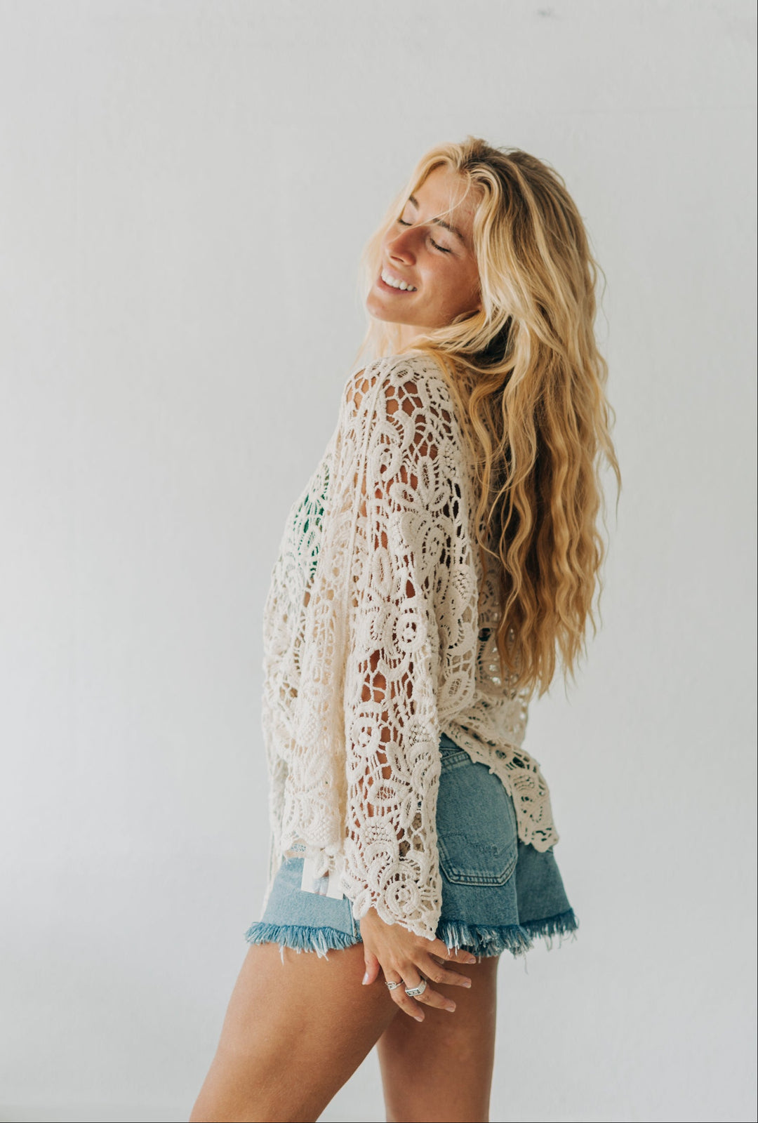 Woman wearing a lace top and denim shorts against a plain background