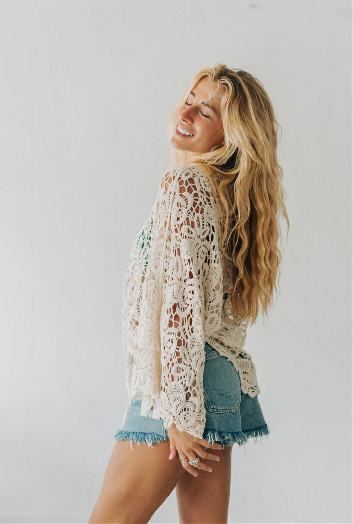 Woman wearing a lace top and denim shorts against a plain background