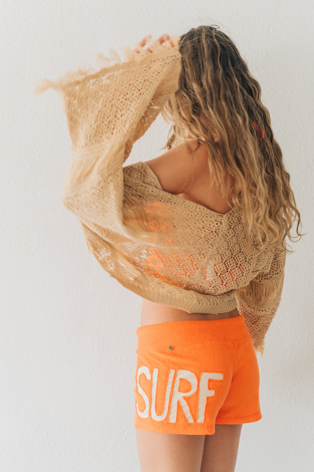 Person wearing a beige cover-up and orange shorts with &