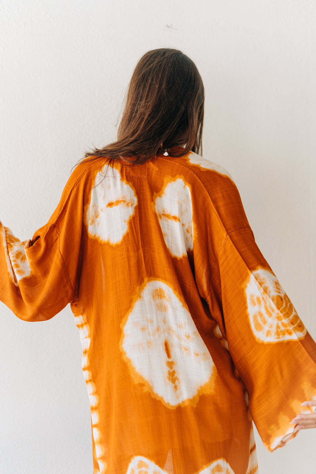 Person wearing an orange and white tie-dye kimono against a white background
