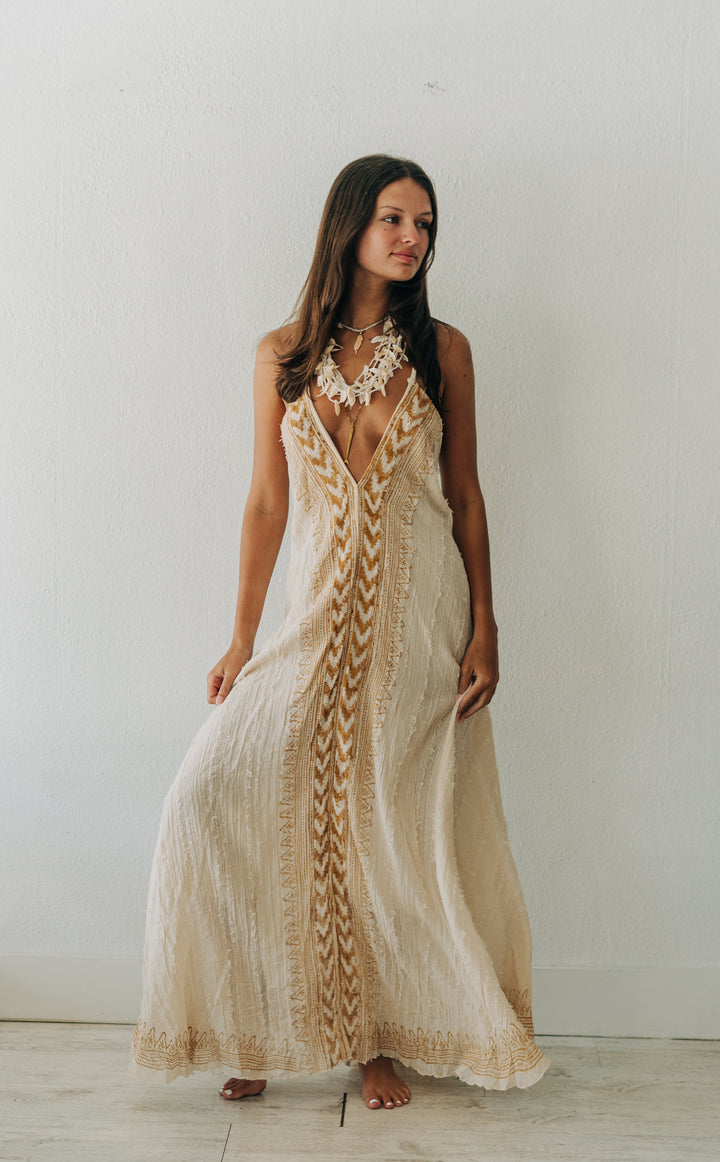 Woman wearing a long, patterned dress against a white wall.