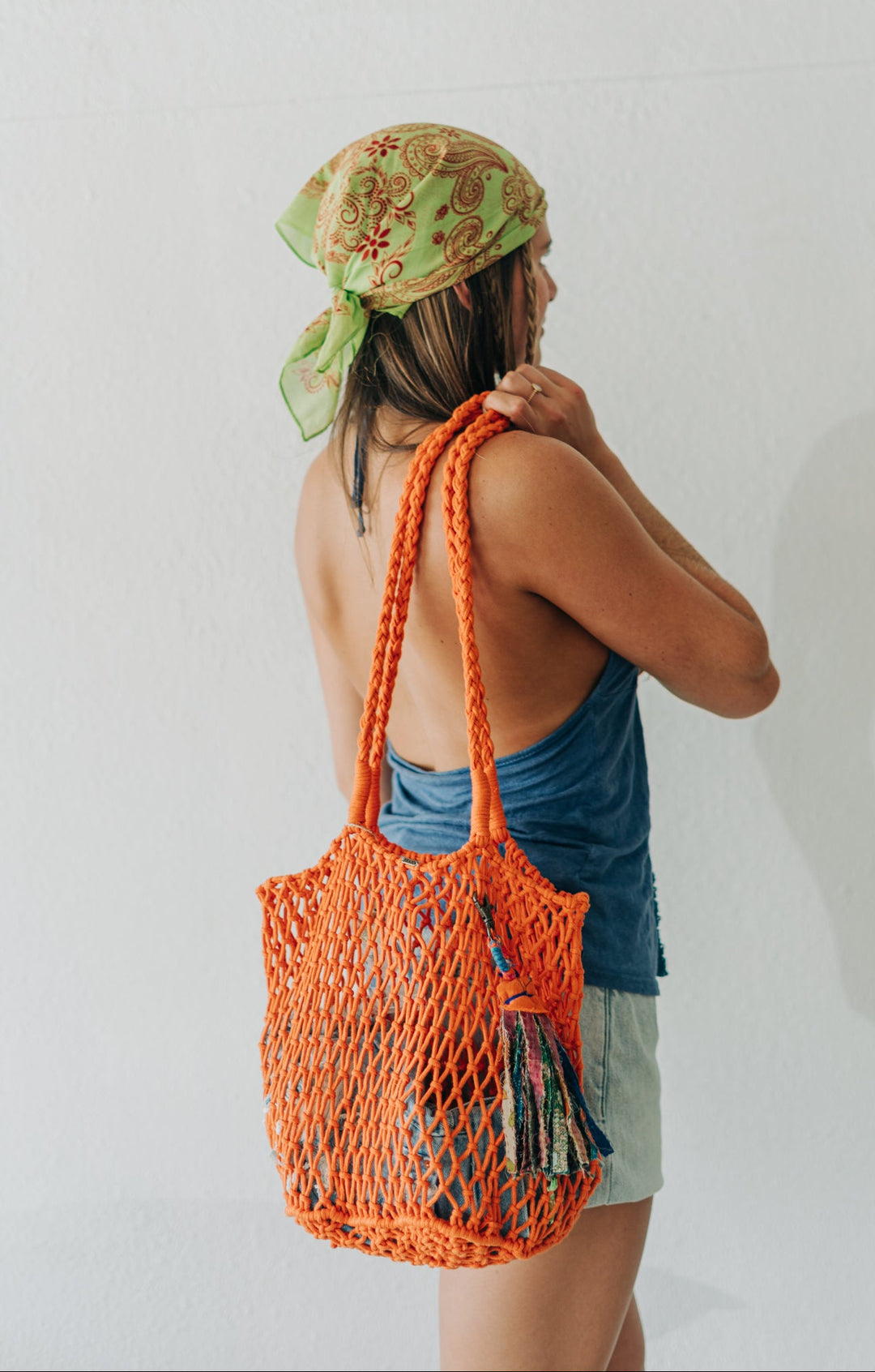 Person wearing a green headscarf and holding an orange mesh bag against a white background