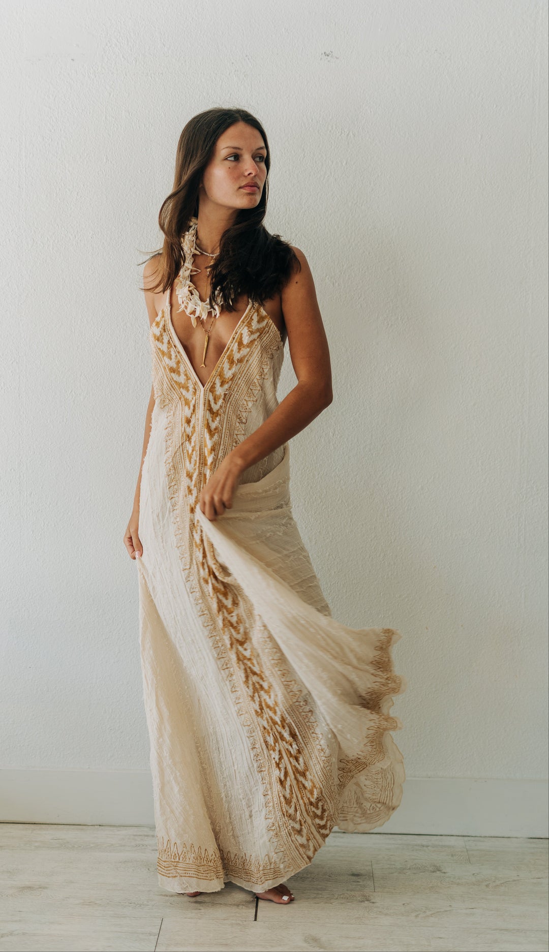 Woman wearing a beige and brown patterned dress against a white wall.