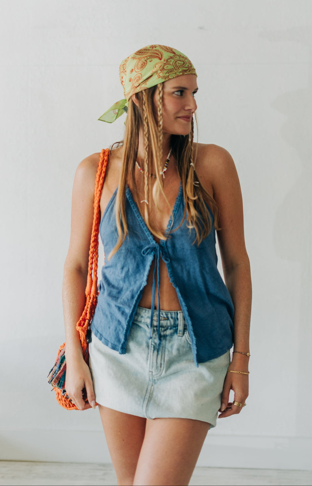 Woman wearing a denim top and light shorts with a colorful bag against a white wall