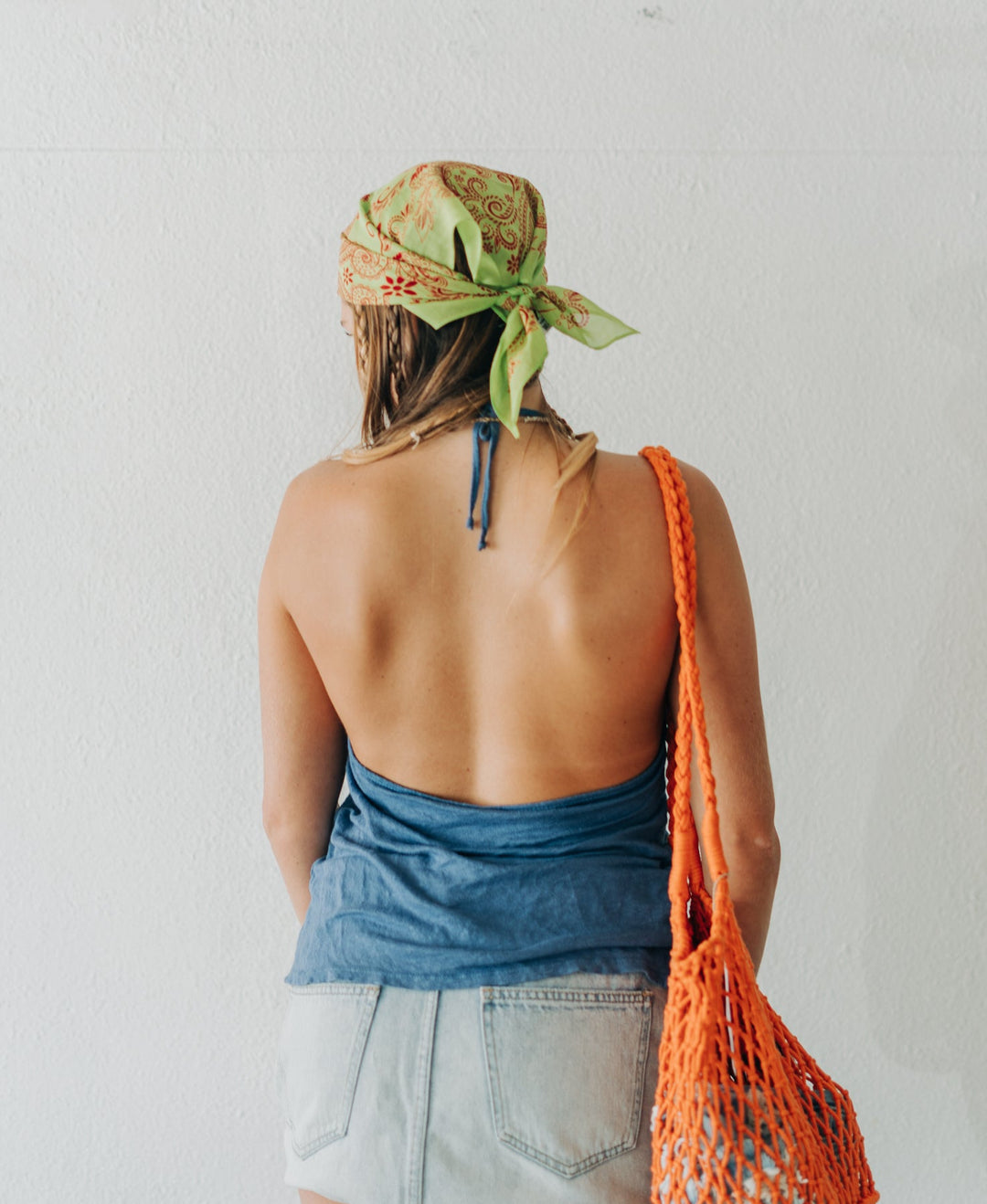 Person wearing a denim top and shorts with an orange bag, standing against a plain background