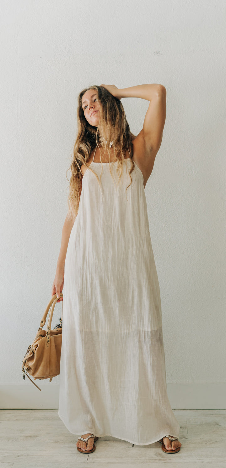 Woman in a white dress holding a brown handbag against a plain white wall.