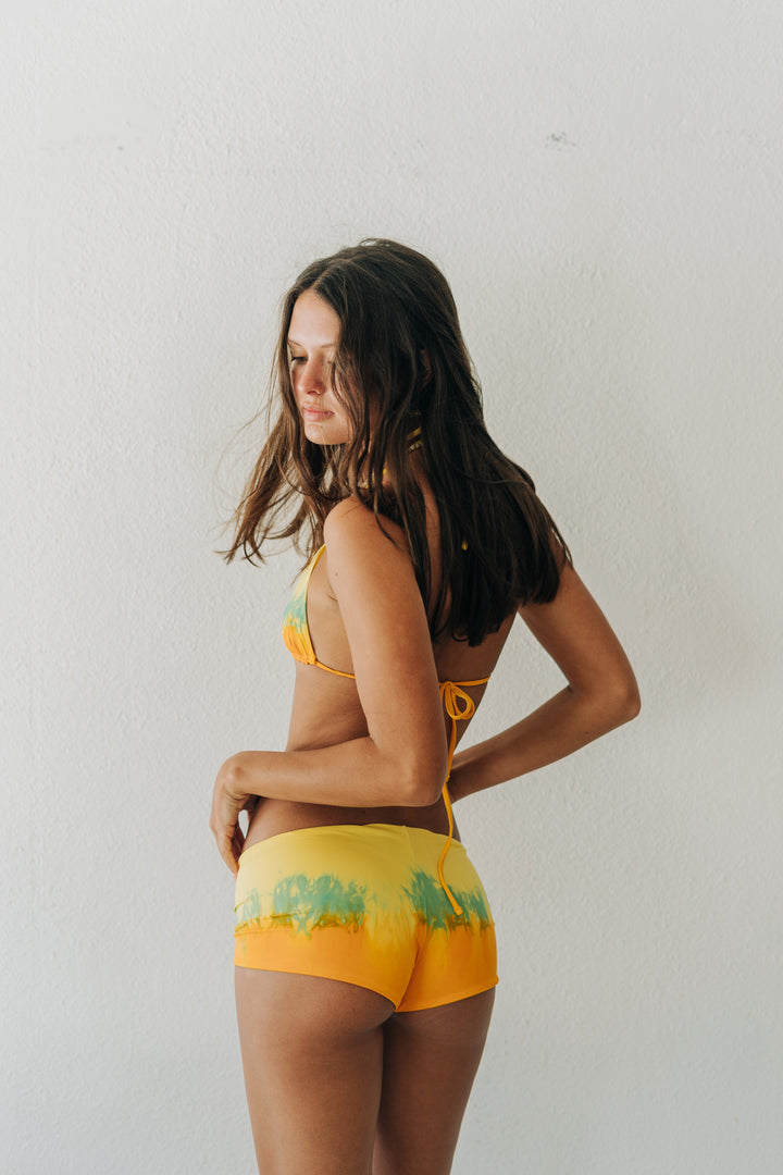 Woman wearing a yellow bikini with green patterns against a white background