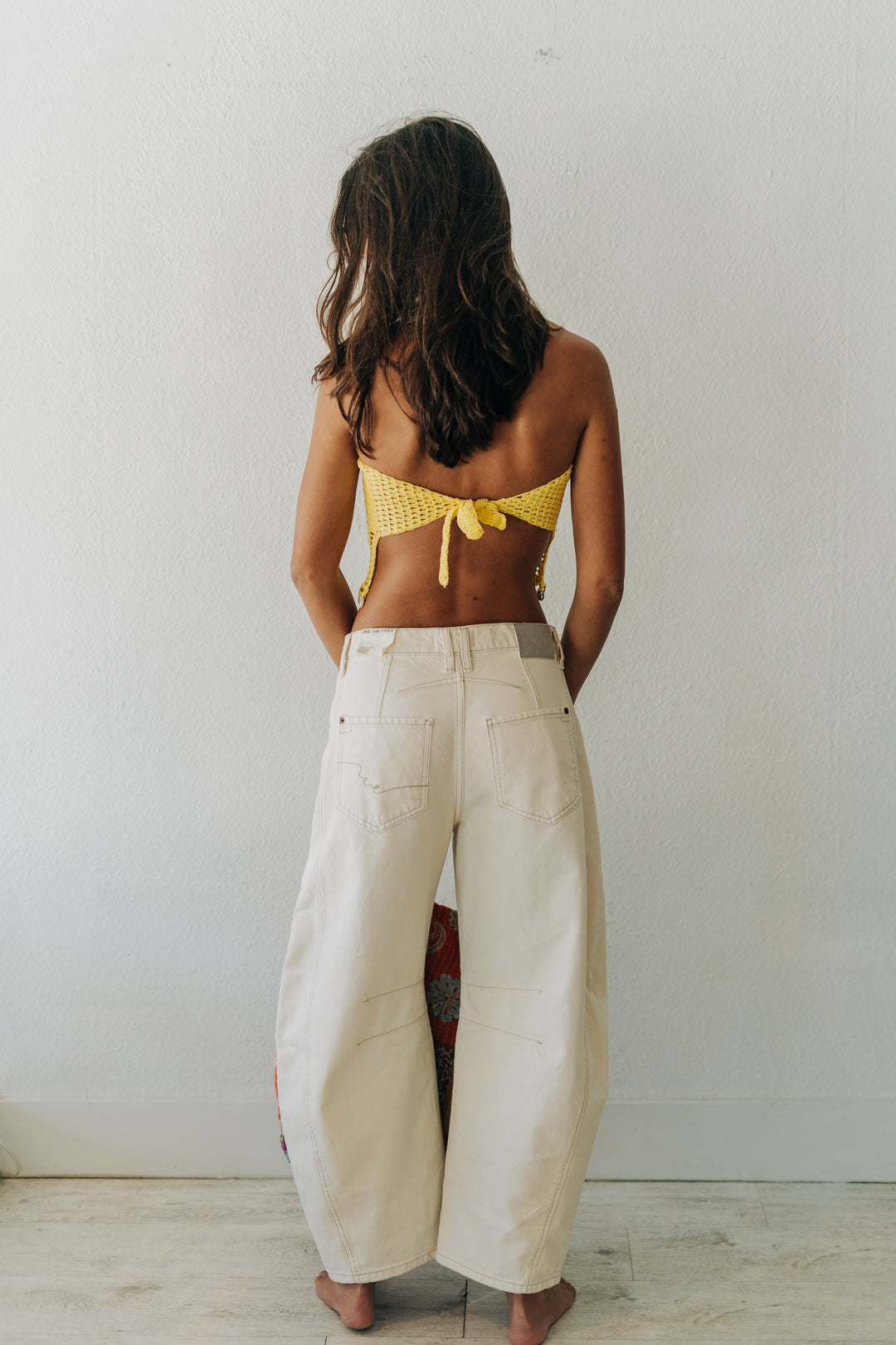 Person wearing a yellow bikini top and white pants against a plain background