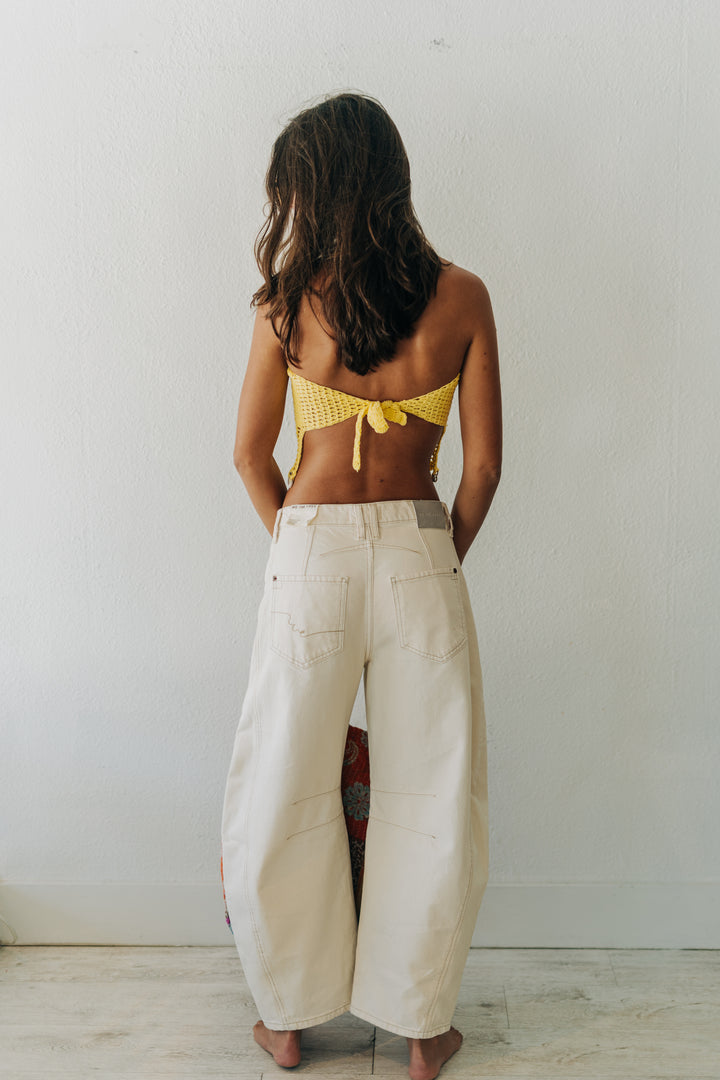 Person wearing a yellow bikini top and white pants against a plain background