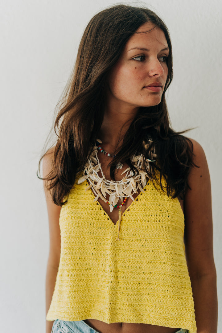 Woman wearing a yellow top with a white lace collar against a plain background