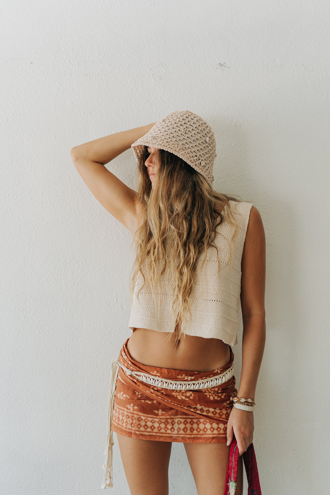 Woman wearing a beige sleeveless top and patterned skirt against a white wall.