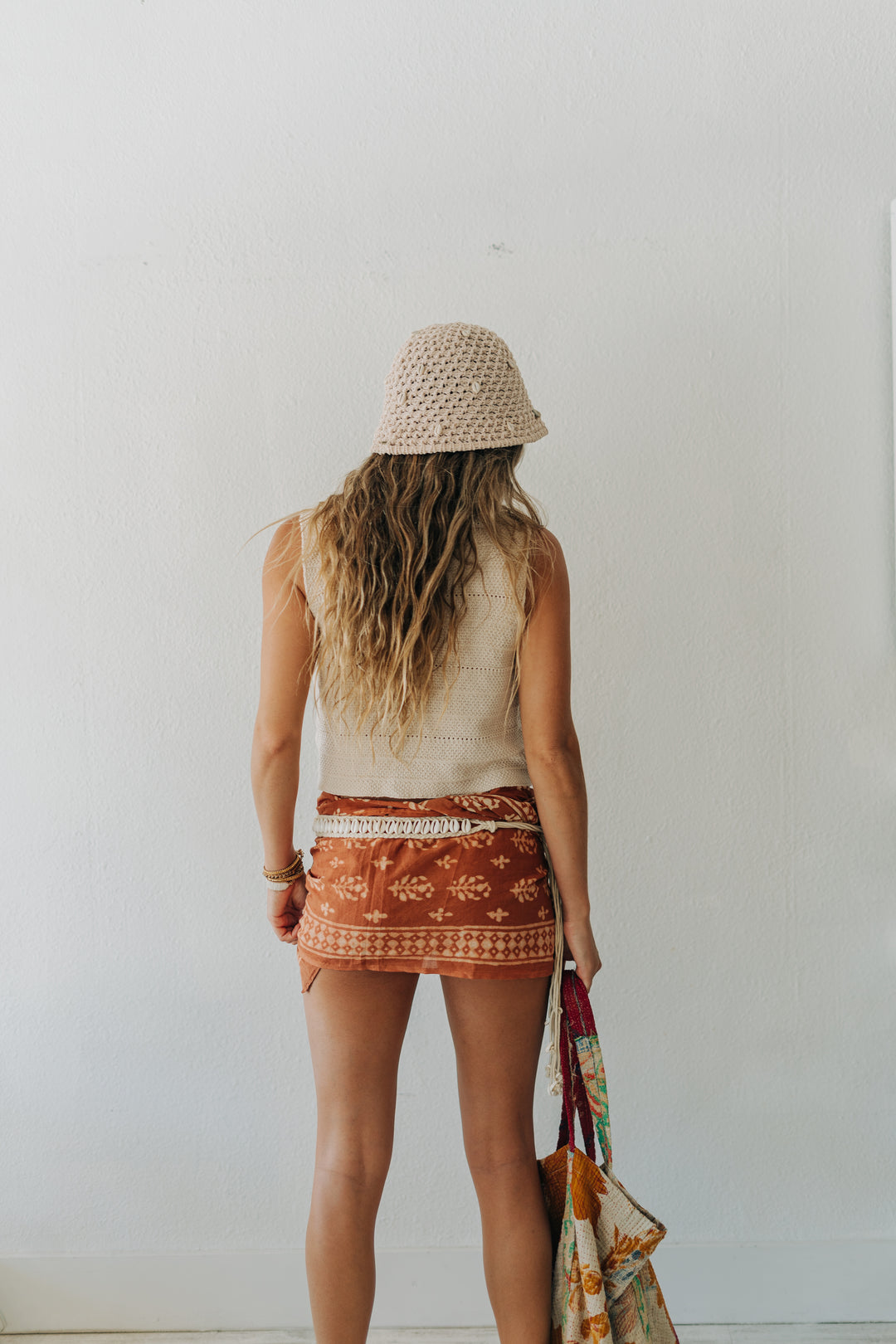 Woman wearing a white sleeveless top and patterned shorts, standing against a plain white wall.