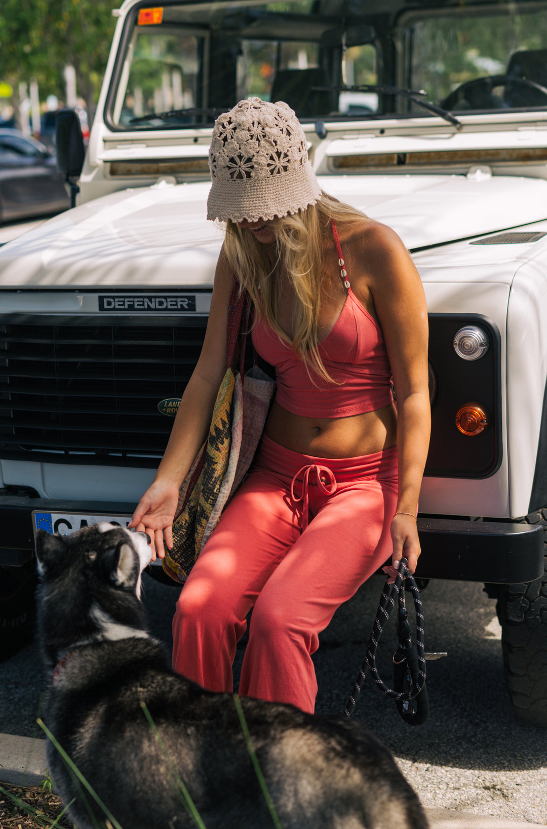 Woman in pink outfit sitting on a dog in front of a Land Rover Defender