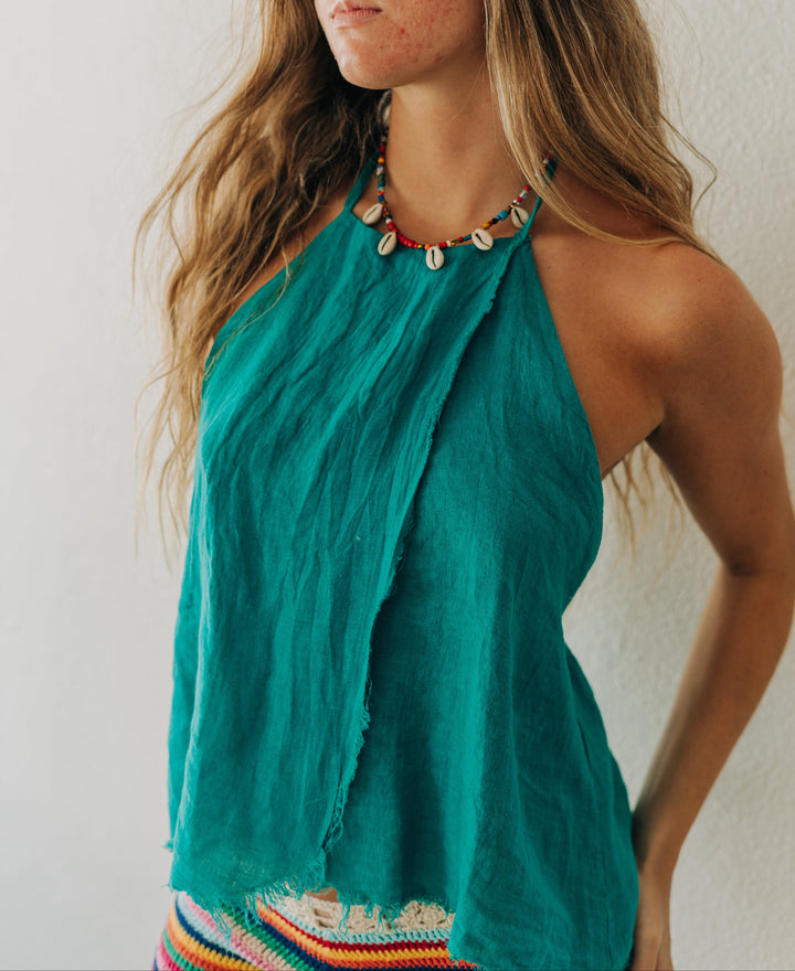 Woman wearing a teal halter top with colorful embroidery against a white wall