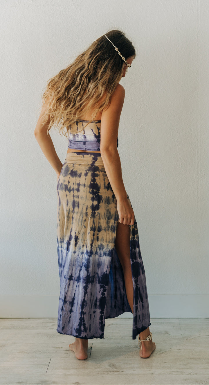 Woman wearing a tie-dye dress standing against a white wall.