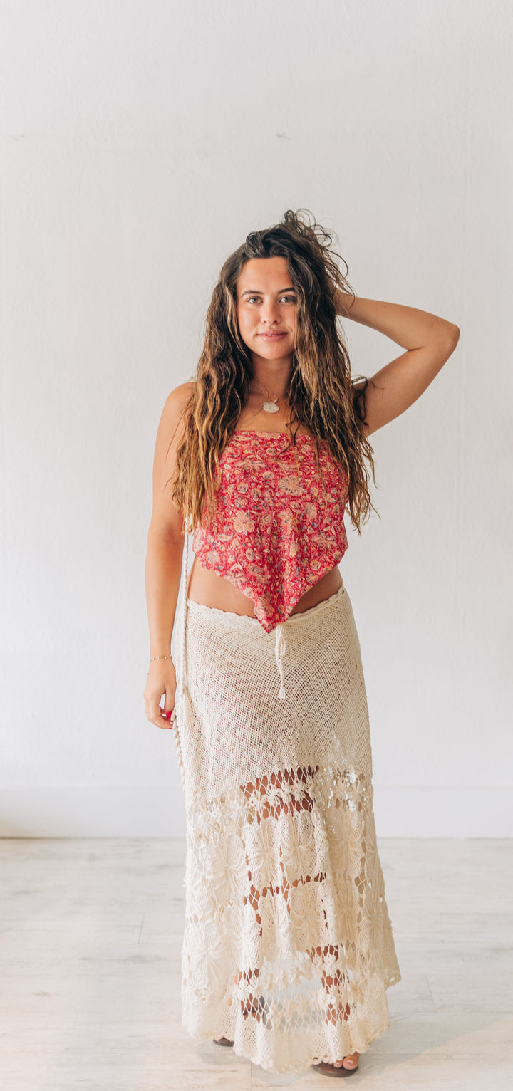 Woman wearing a red floral top and beige skirt standing in a room with white walls.