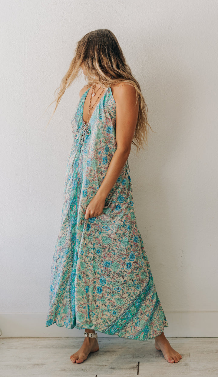 Woman wearing a floral dress standing against a white wall.