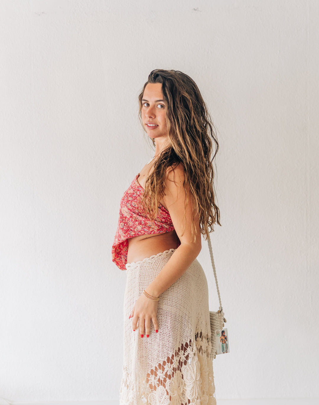 Woman wearing a red top and beige skirt standing against a white wall.