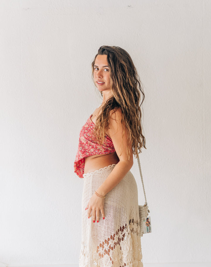 Woman wearing a red top and beige skirt standing against a white wall.