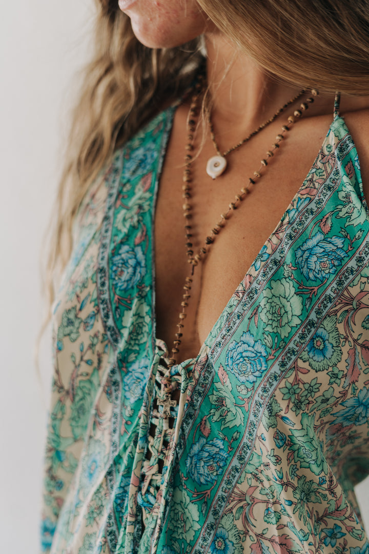Close-up of a person wearing a patterned dress with a necklace against a neutral background
