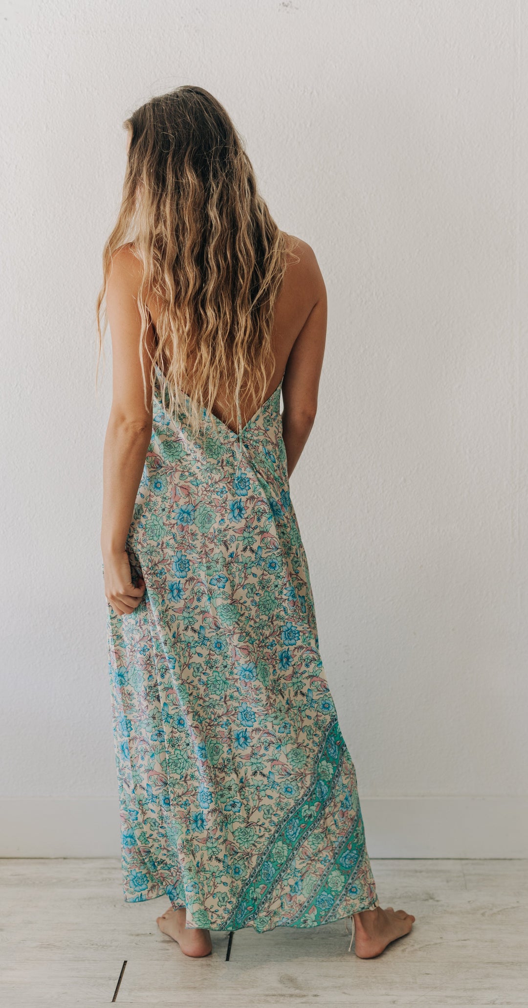 Woman wearing a floral dress standing against a white wall.