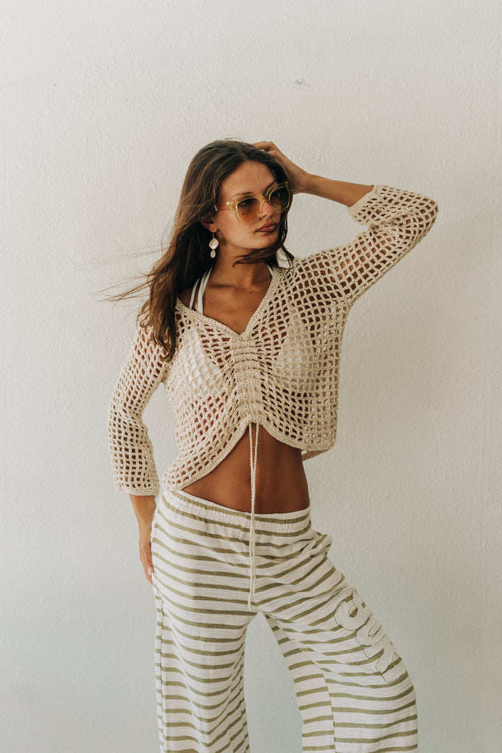Woman wearing a crochet top and striped pants against a plain background